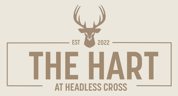A minimalist logo design featuring a deer head with antlers above the text 'THE HART' and 'AT HEADLESS CROSS', with 'EST 2022' centered on a light beige background.