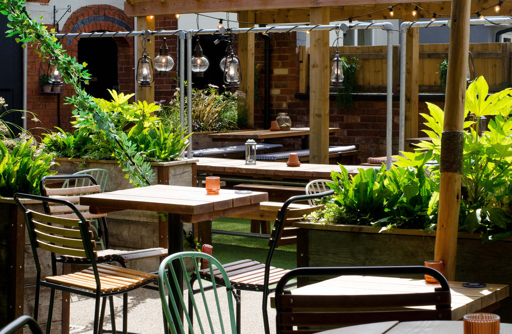 Spacious outdoor courtyard at The Hart in Headless Cross, Redditch, with multiple dining tables, varied seating, garden planters and a timber pergola.