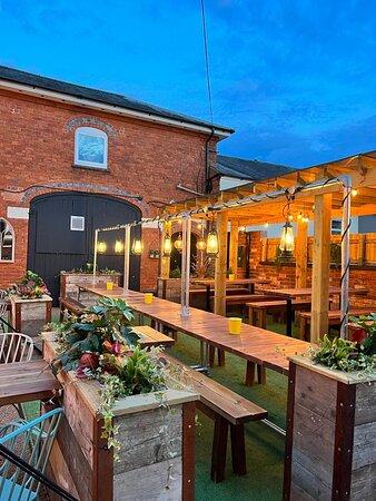 Spacious outdoor courtyard at The Hart in Headless Cross, Redditch, with multiple dining tables, varied seating, garden planters and a timber pergola.