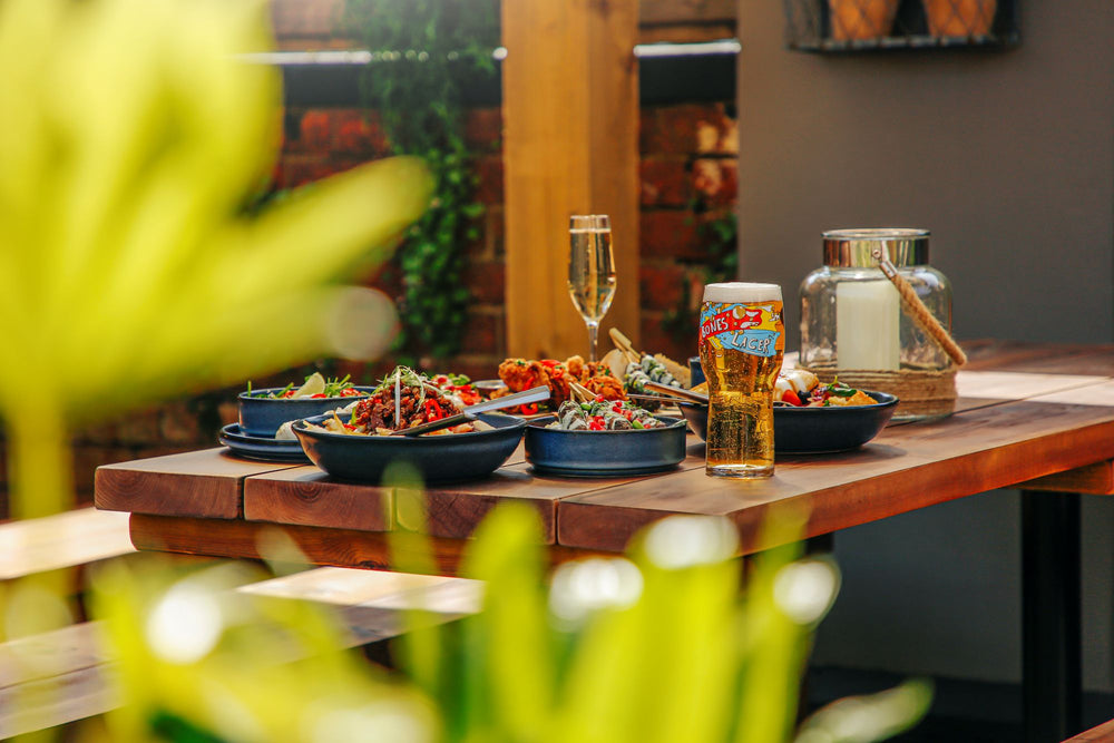 Plates of food and a pint of beer on an outdoor wooden table at The Hart in Redditch, showcasing pub dining in the garden.