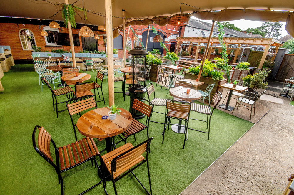 Wide view of the outdoor beer garden at The Hart in Headless Cross, Redditch, with wooden dining tables, mixed garden seating, raised planters and a covered pergola.
