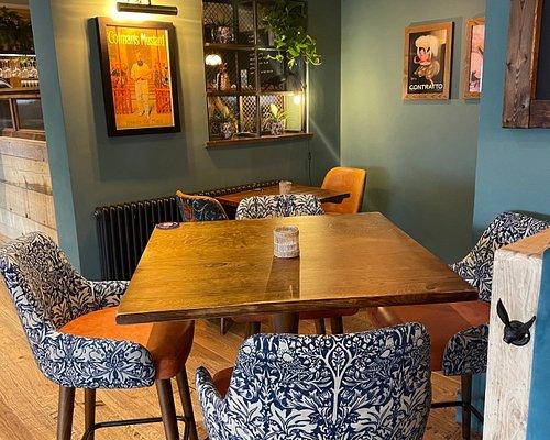 Restaurant dining area at The Hart pub in Headless Cross, Redditch, featuring wooden dining tables, leather banquette seating, upholstered chairs, warm lighting and large front windows.