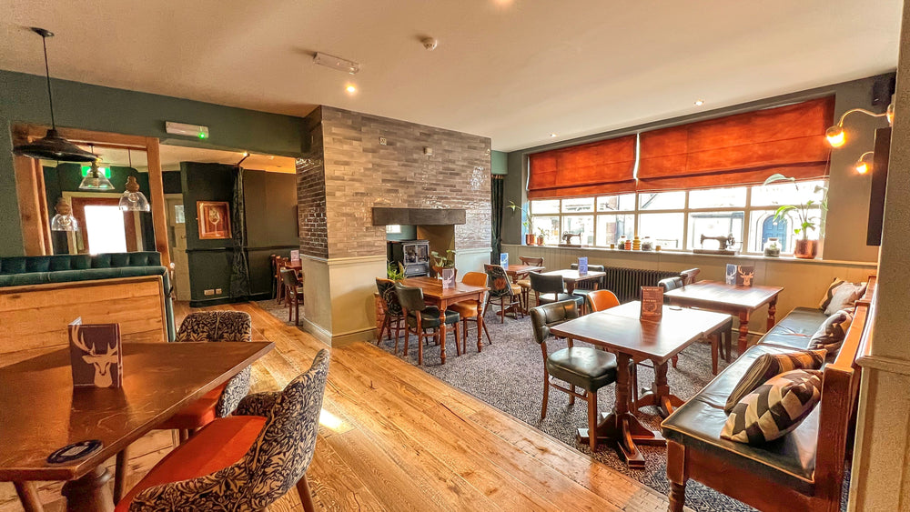 Restaurant dining area at The Hart pub in Headless Cross, Redditch, featuring wooden dining tables, leather banquette seating, upholstered chairs, warm lighting and large front windows.