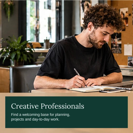 Creative professional sketching in a notebook beside a laptop in a studio-style co-working space with a pinboard