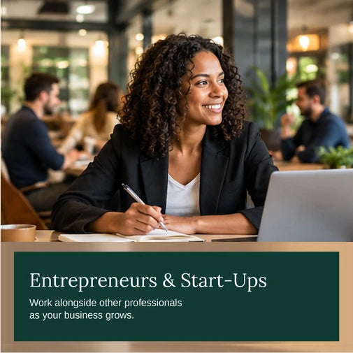 Entrepreneur smiling and taking notes beside a laptop in a busy shared workspace