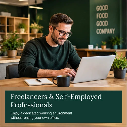 Freelancer working on a laptop at a wooden table in a co-working space with green walls and plants