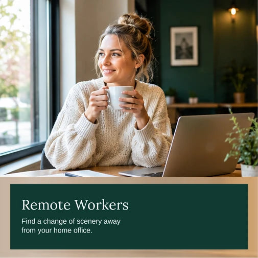 Remote worker enjoying a coffee beside a window in a bright co-working space with a laptop and notebook
